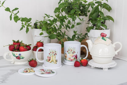 White ceramic mugs with floral designs, a teapot, and strawberries on a white surface with plants in the background.