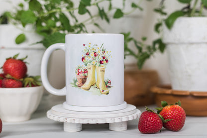 White mug with floral and boot design on a decorative stand, surrounded by strawberries and plants.