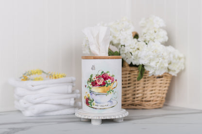 Decorative tissue holder with floral design on a surface with flowers and towels in the background