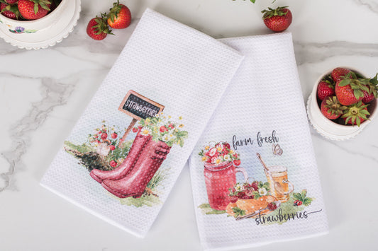 Two kitchen towels with strawberry-themed designs on a marble surface.